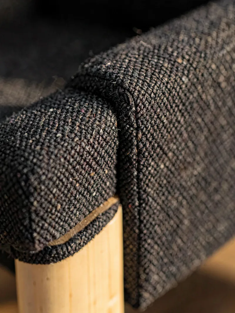 Close detail of an upholstered armchair's woven fabric meeting its pale timber leg