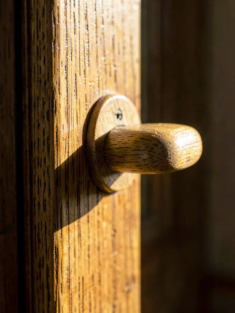 A pale oak door handle set into a stained timber doorframe