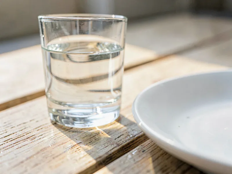 A plain glass of water beside the edge of a white plate